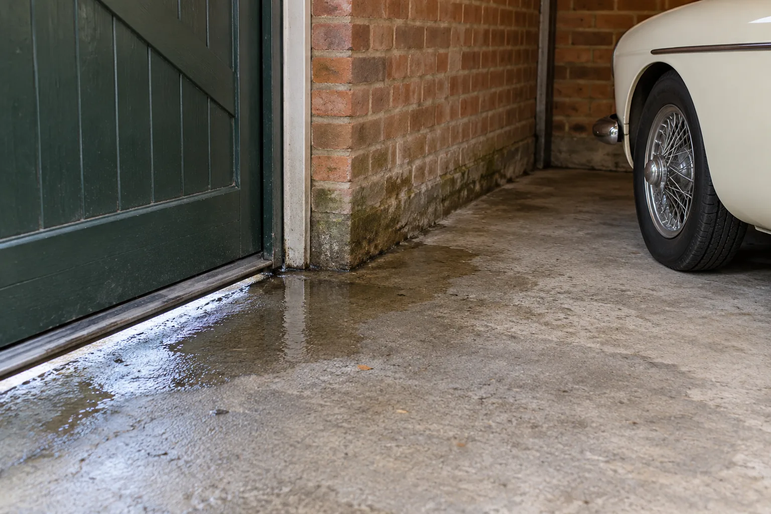Illustration of damp concrete by a green garage door beside a stored classic car